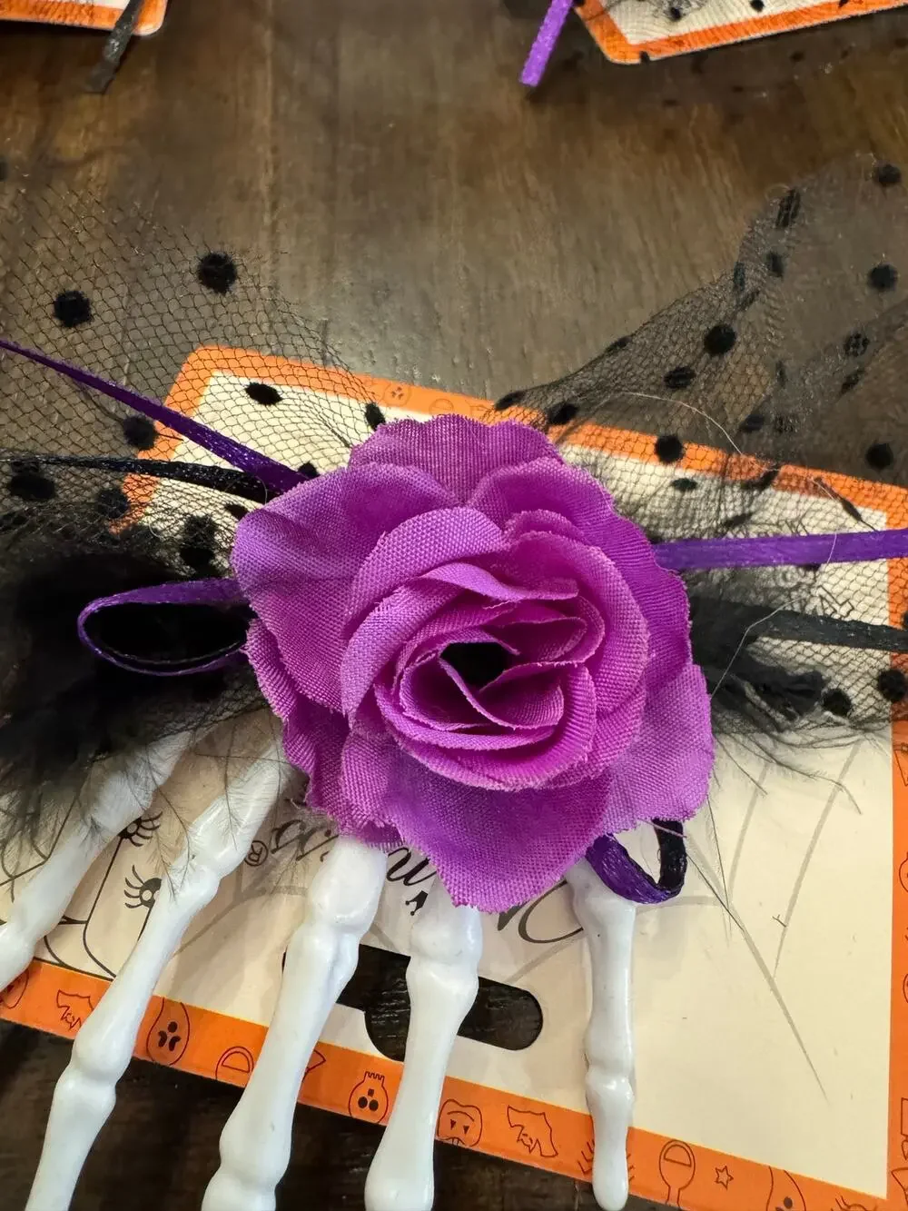 Purple rose hair clip with black netting and purple ribbon on a skeleton hand
